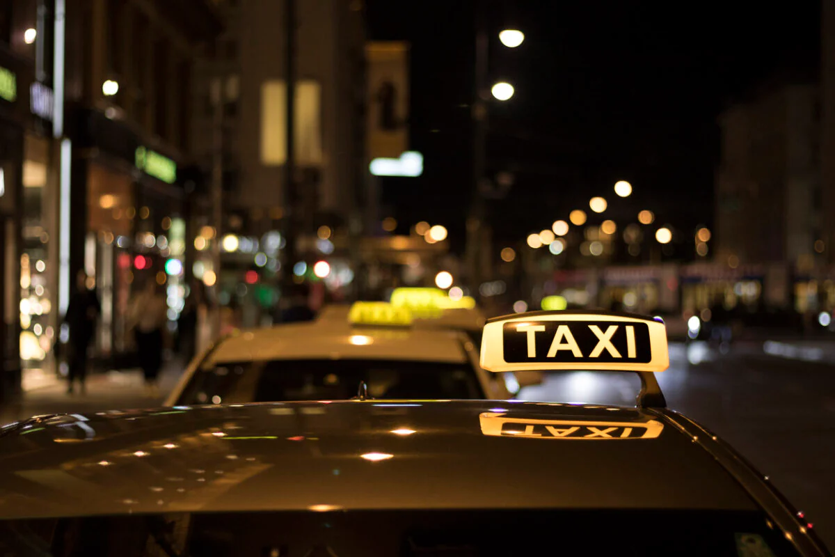 Mehrere Taxis stehen in einer Reihe, wobei man beim vordersten Fahrzeug den Schriftzug gut erkennen kann