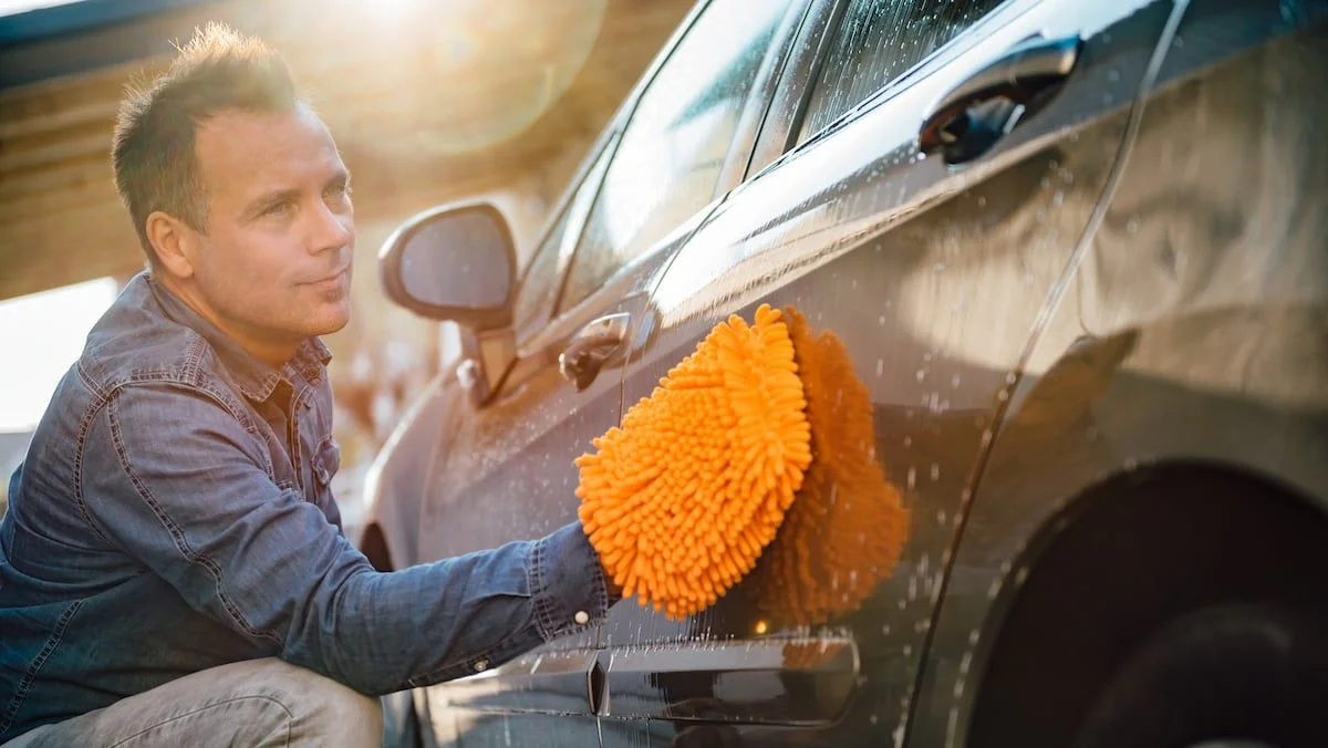 Mann beim Auto waschen mit oragenem Lappen