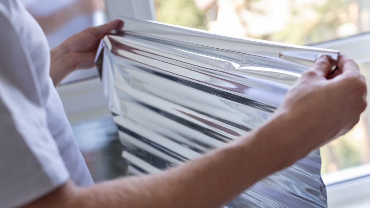 Mann hält Alufolie vor ein Fenster gegenh Hitze