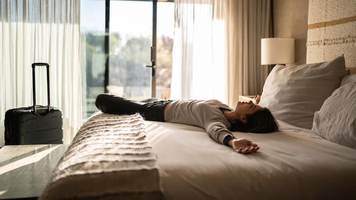 Frau liegt in einem Hotelzimmer auf dem Bett, am Fußende sieht man einen Bettschal aus Wolle