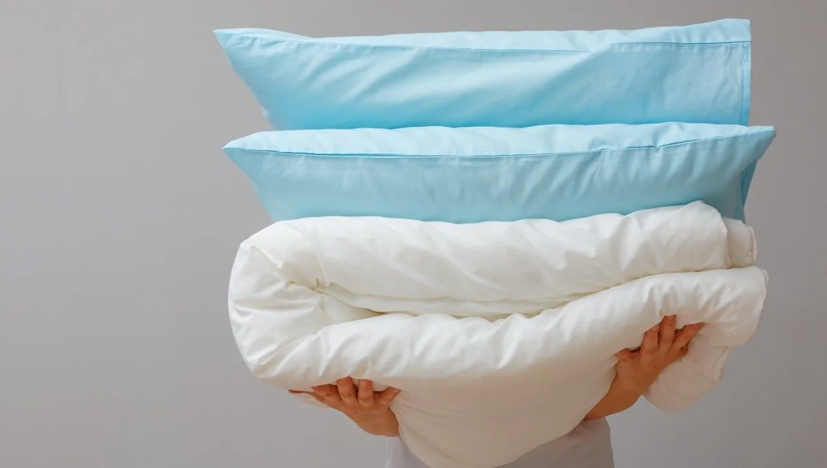 Bettwäsche: Person trägt gestapelte Kissen und Decke auf den Armen