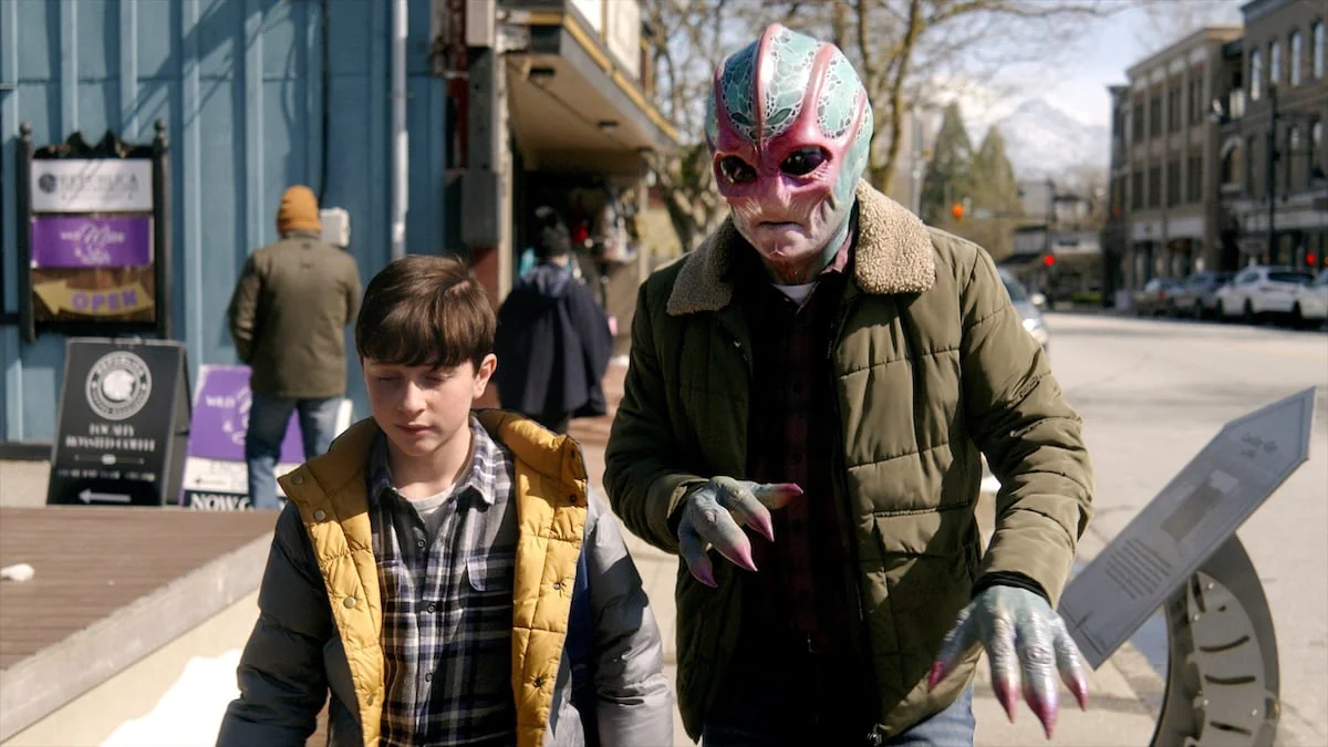 Szene der Sci-Fi-Serie „Resident Alien“, in der ein Alien neben einem Jungen auf der Straße läuft
