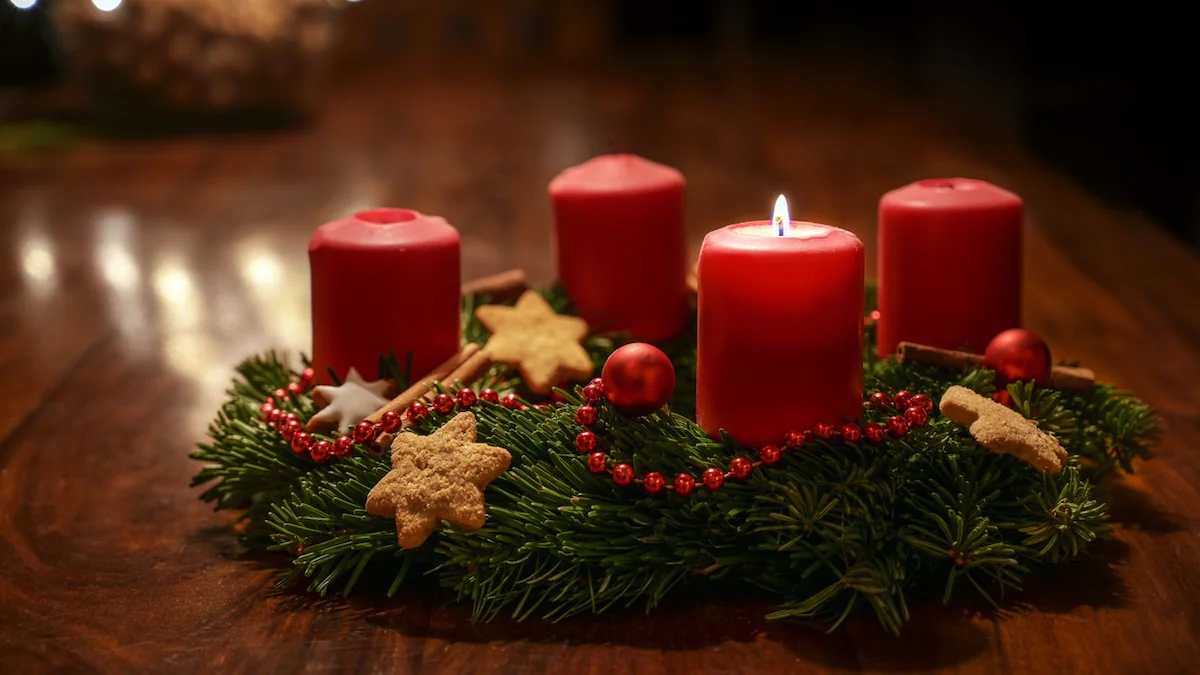 Vier Adventskerzen auf einem Kranz, von denen eine brennt