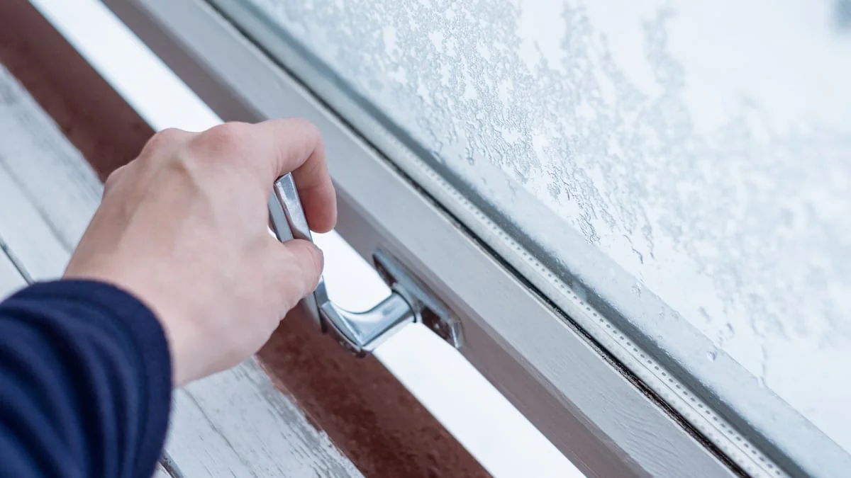 Jemand öffnet ein Fenster mit Eiskristallen, um zu Lüften