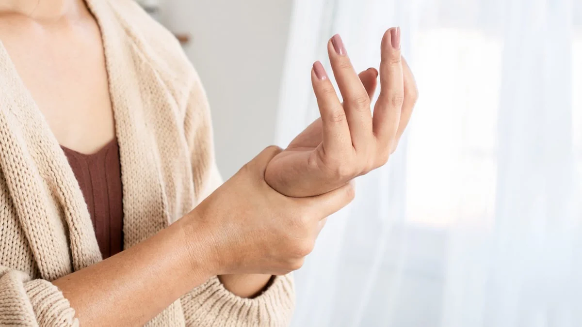 Schlafposition T-Rex-Arme: Frau reibt sich schmerzende Handgelenke