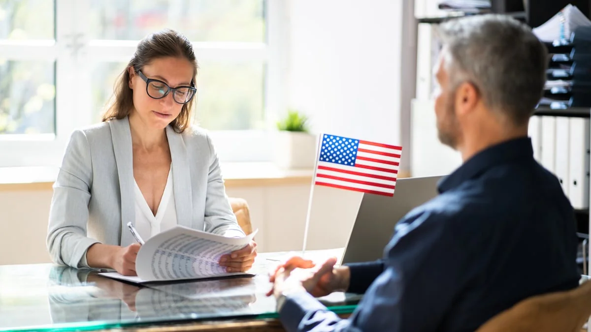 Interviewsituation bei der USA-Einreise: Mann mit USA-Fähnchen sitzt einer Frau gegenüber