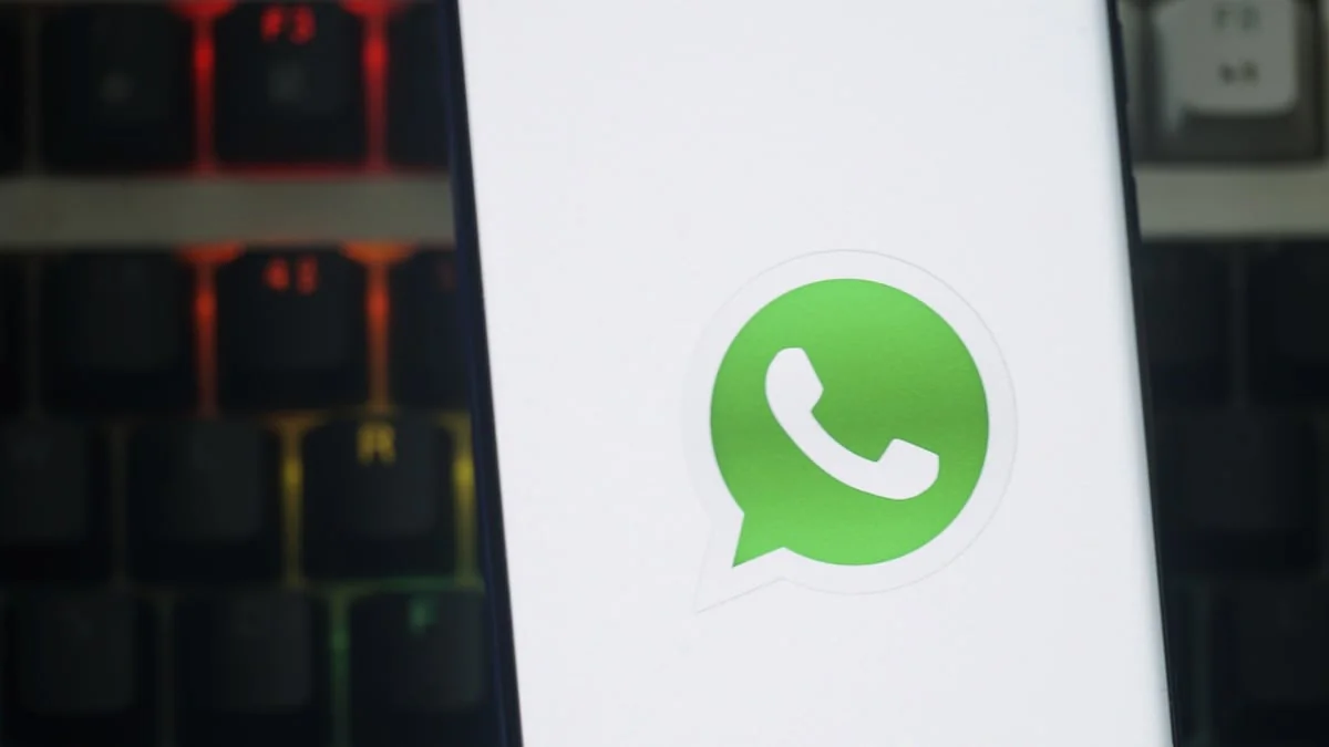 Vor einer verschwommenen Tastatur im Hintergrund ist vor eine Smartphone zu sehen, das das Logo des Messengers WhatsApp zeigt